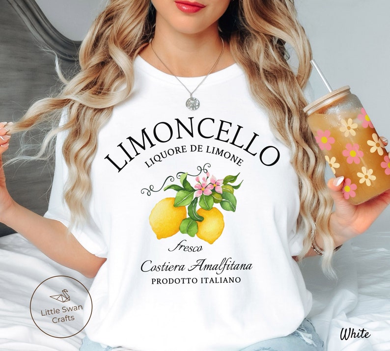 May include: White t-shirt with a graphic design of lemons and flowers. The text reads "Limoncello Liquore de Limone Fresco Costiera Amalfitana Prodotto Italiano".