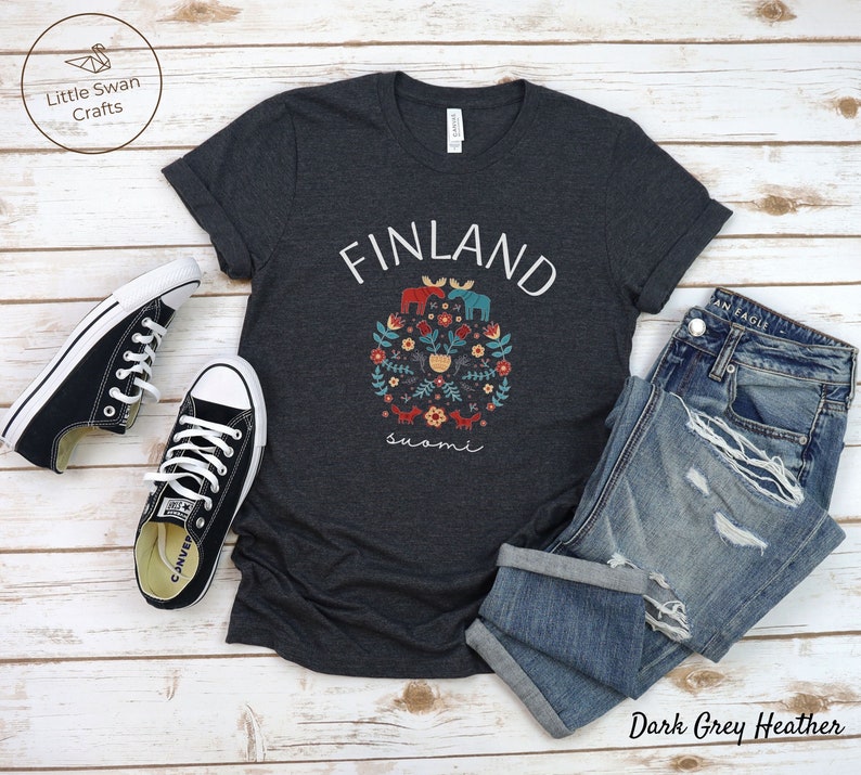 May include: Dark grey heather t-shirt with a white graphic of a floral design with the word "FINLAND" above it and the word "suomi" below it. The graphic features a moose, a fox, a bear, and a bird.