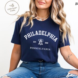 May include: A navy blue t-shirt with a white graphic of the Liberty Bell and the text "PHILADELPHIA EST. 1682 PENNSYLVANIA".