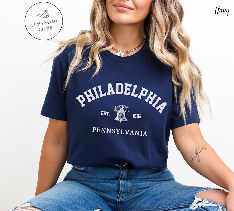 May include: A navy blue t-shirt with a white graphic of the Liberty Bell and the text "PHILADELPHIA EST. 1682 PENNSYLVANIA".