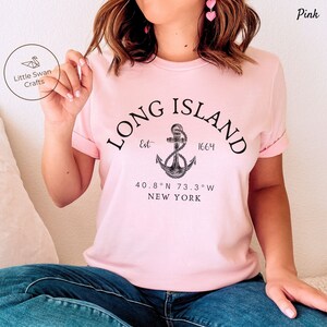 Op de afbeelding: Roze T-shirt met een zwart grafisch ontwerp met een anker en de tekst "LONG ISLAND Est. 1664 40.8&deg;N 73.3&deg;W NEW YORK"