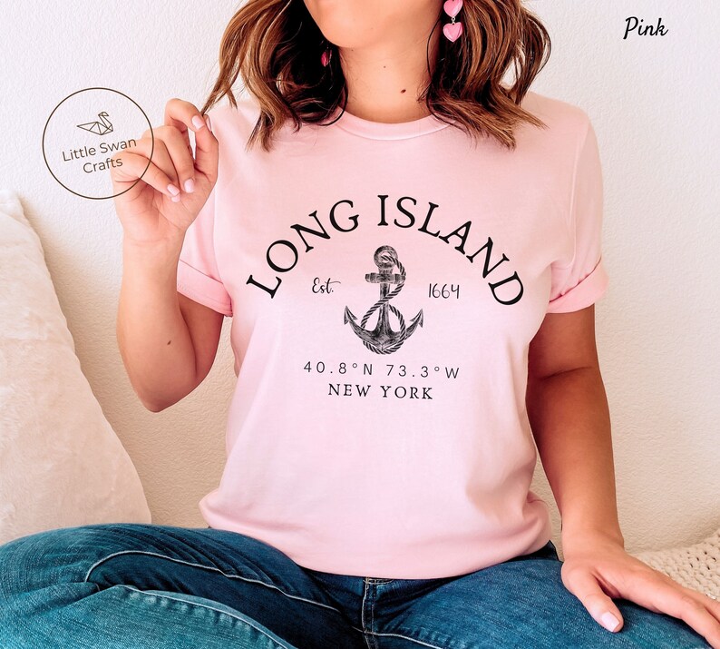 Op de afbeelding: Roze T-shirt met een zwart grafisch ontwerp met een anker en de tekst "LONG ISLAND Est. 1664 40.8&deg;N 73.3&deg;W NEW YORK"
