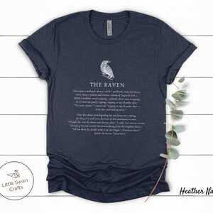 Puede incluir: Camiseta azul marino jaspeado con una ilustraci&oacute;n de cuervo blanco y texto del poema "El Cuervo" de Edgar Allan Poe. El texto dice: "Once upon a midnight dreary, while I pondered, weak and weary..."