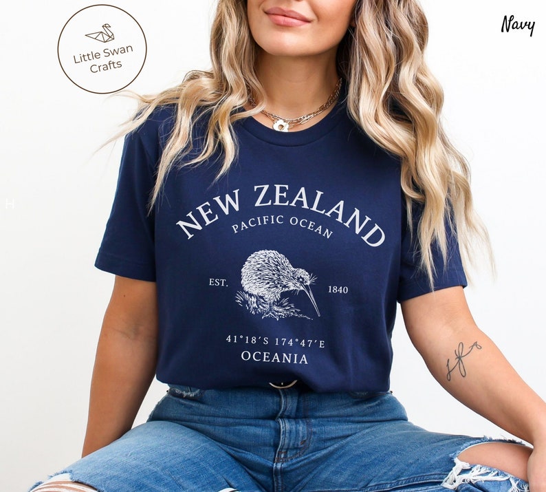 Peut inclure: T-shirt bleu marine avec un graphique blanc d'un kiwi et le texte "NEW ZEALAND, PACIFIC OCEAN, EST. 1840, 41&deg;18&prime;S 174&deg;47&prime;E, OCEANIA".