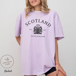 Pode incluir: T-shirt lil&aacute;s claro com a palavra "SCOTLAND" em preto em forma de arco. Abaixo, um bras&atilde;o e as palavras "UNITED KINGDOM". A t-shirt tem um corte folgado.