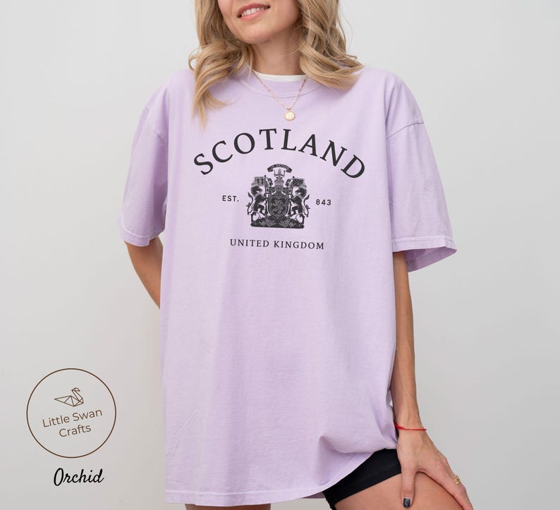 Pode incluir: T-shirt lil&aacute;s claro com a palavra "SCOTLAND" em preto em forma de arco. Abaixo, um bras&atilde;o e as palavras "UNITED KINGDOM". A t-shirt tem um corte folgado.