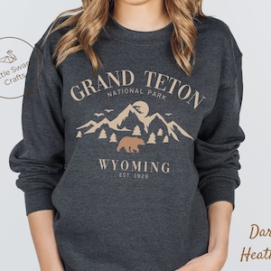 May include: Dark heather grey sweatshirt with a graphic design of a mountain range, a bear, and the text "Grand Teton National Park, Wyoming Est. 1929."