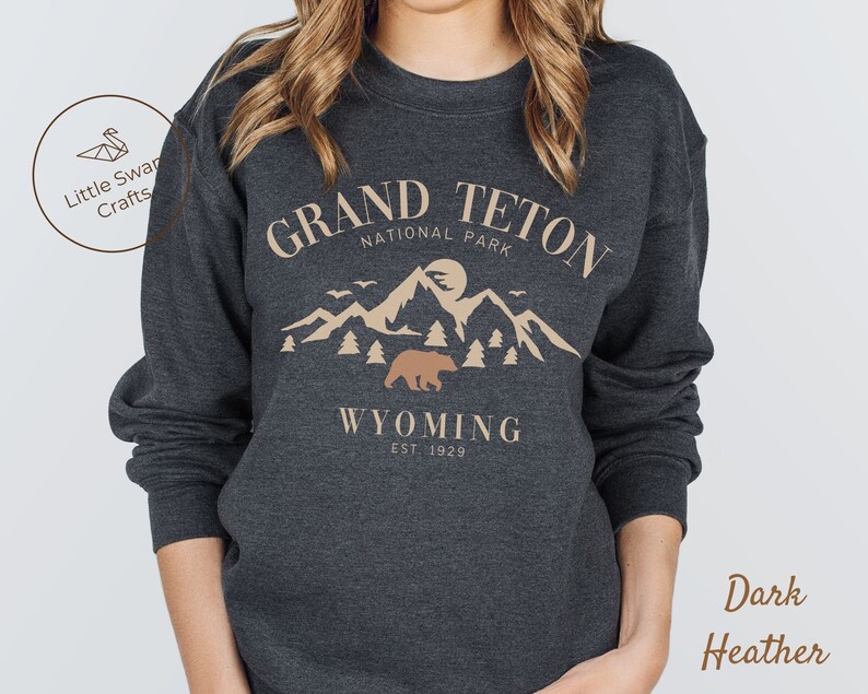 May include: Dark heather grey sweatshirt with a graphic design of a mountain range, a bear, and the text "Grand Teton National Park, Wyoming Est. 1929."