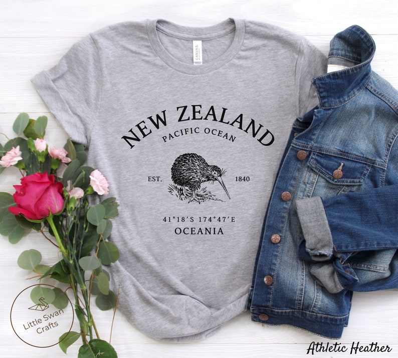 Peut inclure: T-shirt gris avec un graphique noir d'un kiwi et le texte "NEW ZEALAND PACIFIC OCEAN EST. 1840 41&deg;18&prime;S 174&deg;47&prime;E OCEANIA"