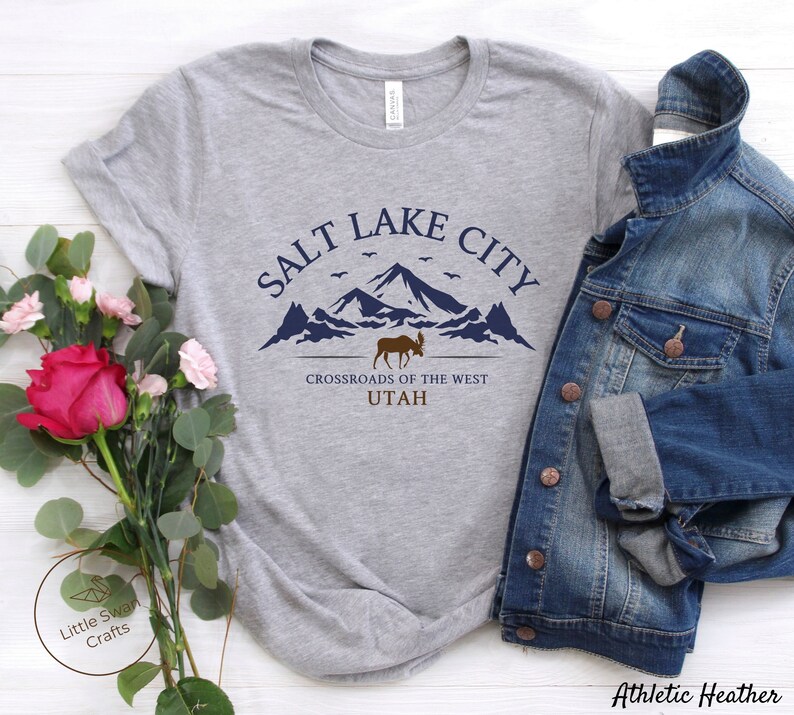 May include: A gray t-shirt with a graphic design featuring a mountain range, a moose, and the text "Salt Lake City, Crossroads of the West, Utah".