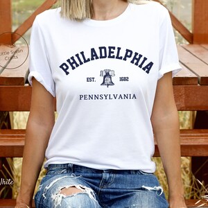 May include: White t-shirt with a blue graphic of the Liberty Bell and the text "PHILADELPHIA EST. 1682 PENNSYLVANIA".