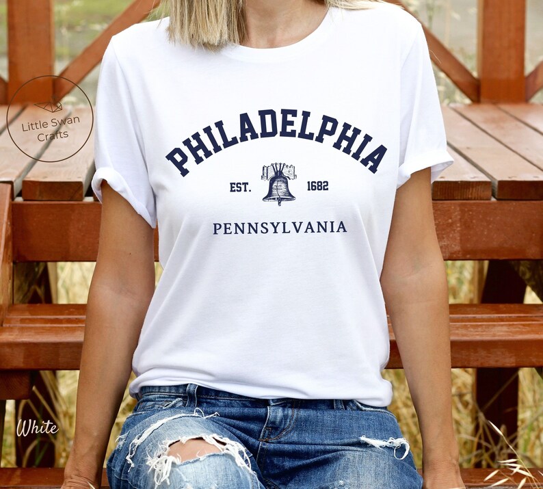May include: White t-shirt with a blue graphic of the Liberty Bell and the text "PHILADELPHIA EST. 1682 PENNSYLVANIA".
