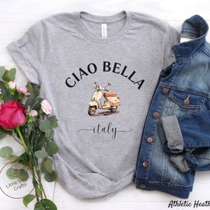 Pu&ograve; includere: Maglietta grigia con il testo "Ciao Bella" e un'illustrazione ad acquerello di uno scooter vintage con la parola "italy" sotto.