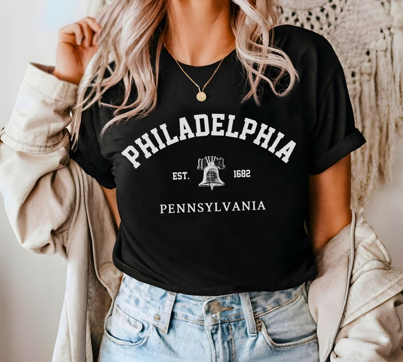 May include: Black t-shirt with white text that reads "Philadelphia Est. 1682 Pennsylvania" with a graphic of a bell.