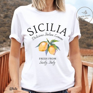 Peut inclure: T-shirt blanc avec un motif graphique qui dit "SICILIA Delicious Italian Lemons Fresh From Sicily, Italy". Le graphique pr&eacute;sente &eacute;galement une illustration aquarelle de citrons sur une branche.