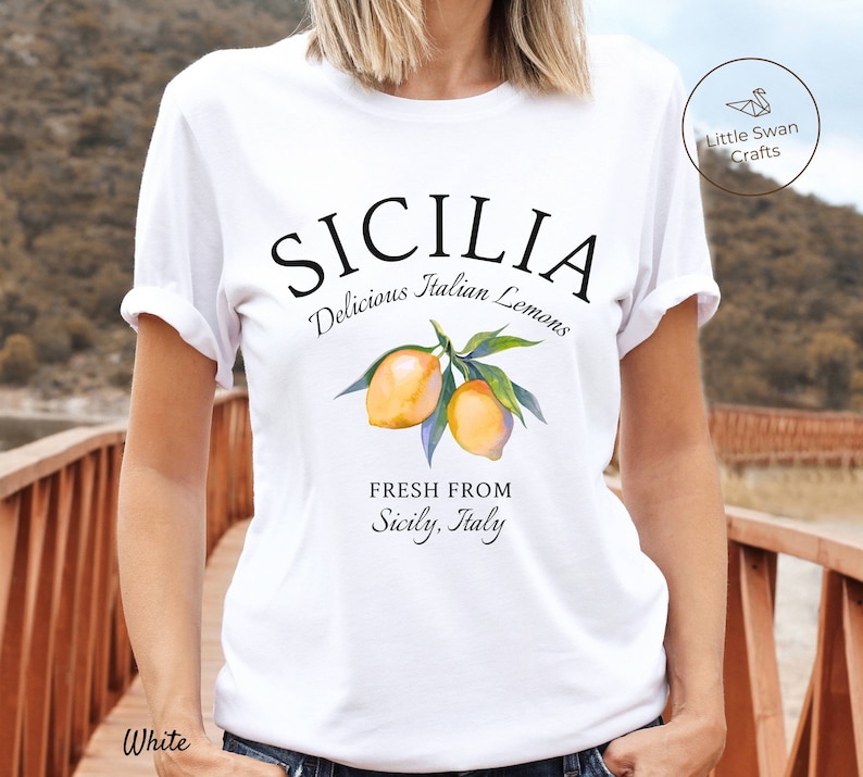 Peut inclure: T-shirt blanc avec un motif graphique qui dit "SICILIA Delicious Italian Lemons Fresh From Sicily, Italy". Le graphique pr&eacute;sente &eacute;galement une illustration aquarelle de citrons sur une branche.