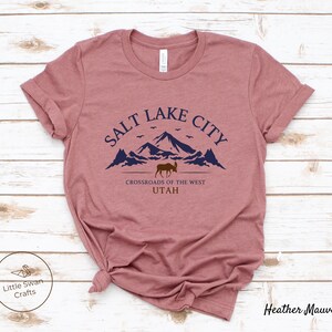 May include: Heather mauve t-shirt with a graphic design of mountains, a moose, and the text "Salt Lake City, Crossroads of the West, Utah".