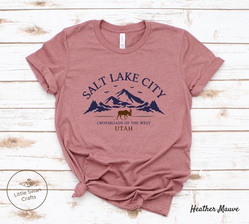 May include: Heather mauve t-shirt with a graphic design of mountains, a moose, and the text "Salt Lake City, Crossroads of the West, Utah".