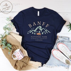 May include: A navy blue t-shirt with a graphic design of mountains, a moose, and the text "BANFF NATIONAL PARK ALBERTA'S ROCKIES CANADA".
