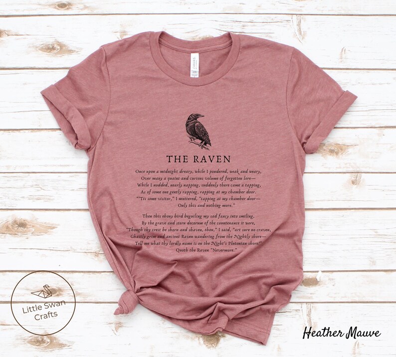 Puede incluir: Una camiseta de color malva brezo con una ilustraci&oacute;n en blanco y negro de un cuervo y el texto "THE RAVEN" y la primera estrofa del poema "El Cuervo" de Edgar Allan Poe.