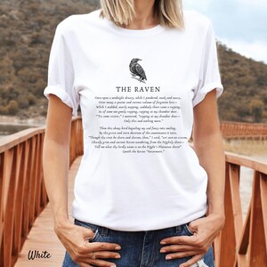 Puede incluir: Camiseta blanca con una ilustraci&oacute;n de cuervo negro y el texto "THE RAVEN" sobre el poema "Once upon a midnight dreary, while I pondered, weak and weary..."