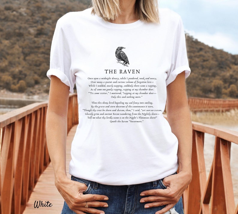 Puede incluir: Camiseta blanca con una ilustraci&oacute;n de cuervo negro y el texto "THE RAVEN" sobre el poema "Once upon a midnight dreary, while I pondered, weak and weary..."