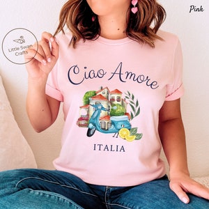 May include: Pink t-shirt with a blue scooter, Italian houses, lemons, and the text "Ciao Amore ITALIA".
