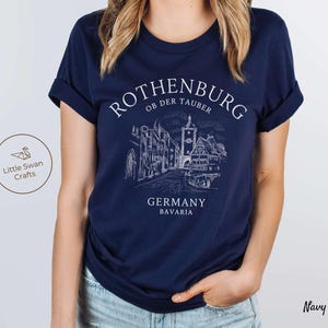 Pode incluir: Camiseta azul marinho com um gr&aacute;fico branco do horizonte de Rothenburg ob der Tauber, Alemanha. O texto "Rothenburg ob der Tauber, Alemanha, Baviera" est&aacute; impresso na camiseta.