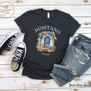 Puede incluir: Camiseta de color gris oscuro jaspeado con un gr&aacute;fico de una puerta azul con flores y un scooter delante. El texto "Positano Italia" est&aacute; impreso debajo del gr&aacute;fico.