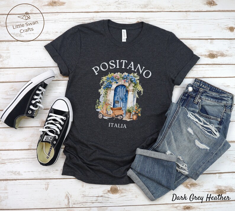 Puede incluir: Camiseta de color gris oscuro jaspeado con un gr&aacute;fico de una puerta azul con flores y un scooter delante. El texto "Positano Italia" est&aacute; impreso debajo del gr&aacute;fico.