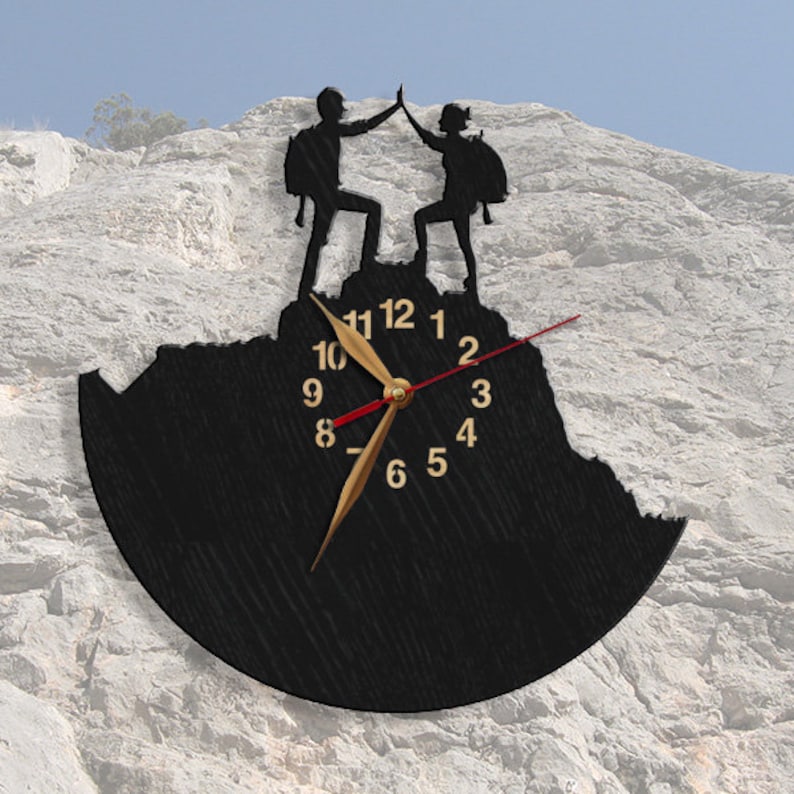 May include: Black wooden wall clock shaped like a mountain with two figures silhouetted on top, giving a high five. The clock face has gold hands and gold numbers.