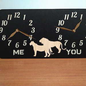 May include: A black wooden clock with two clock faces, each featuring a lion and lioness silhouette. The clock faces are labelled "ME" and "YOU".