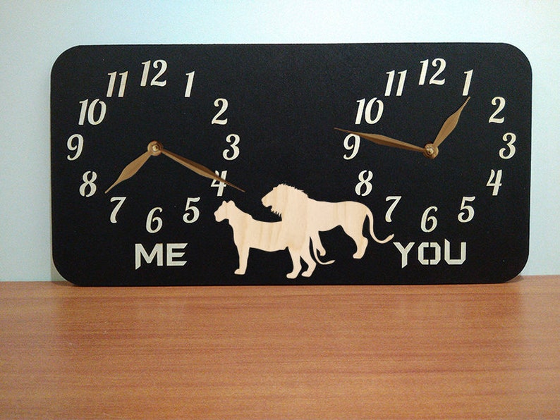 May include: A black wooden clock with two clock faces, each featuring a lion and lioness silhouette. The clock faces are labelled "ME" and "YOU".