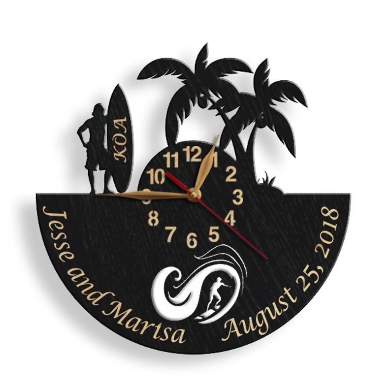 Pu&ograve; includere: Orologio da parete in legno nero a tema surf. Presenta una silhouette di un surfista, palme e una tavola da surf con "KOA". Il quadrante dell'orologio ha lancette e numeri dorati, con i nomi "Jesse and Marisa" e la data "25 agosto 2018".