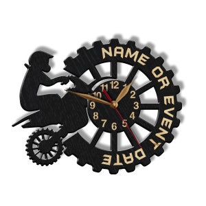 May include: Black wooden clock with a silhouette of a person riding a dirt bike. The clock face has gold numbers and hands. The clock has the words "NAME OR EVENT DATE" around the edge.