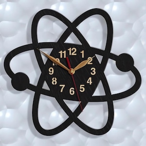 May include: Black wooden clock shaped like an atom with gold numbers and hands. The clock face has the numbers 1 through 12.
