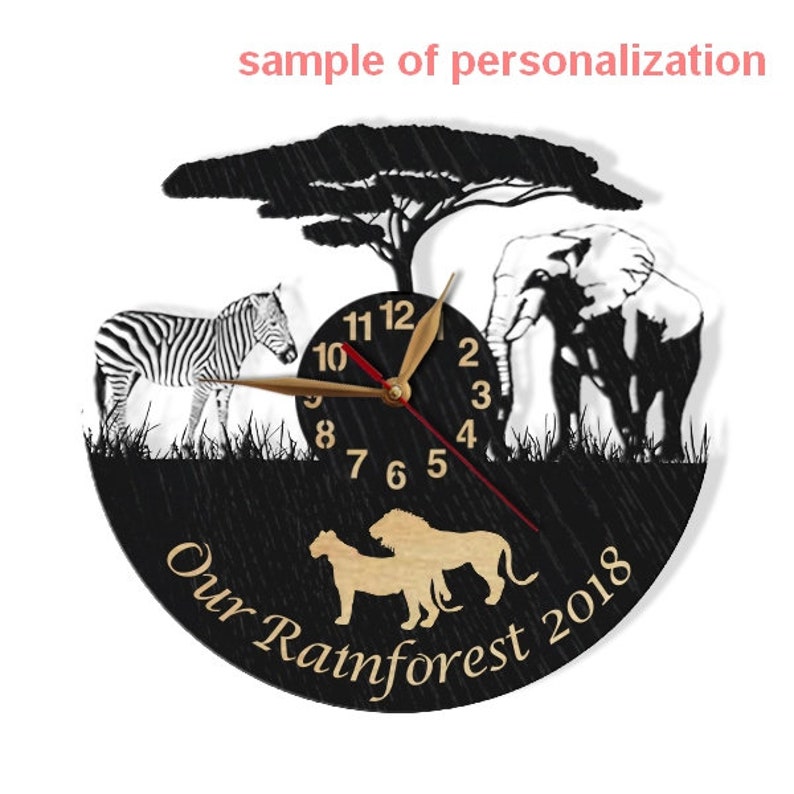 May include: Black wooden clock with a zebra, elephant, lion, and tree silhouette. The clock face has gold hands and black numbers. The clock has the text "Our Rainforest 2018" on the bottom.