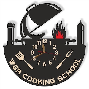 May include: Black and white silhouette of a grill with a clock face in the center. The clock face has Roman numerals and gold hands. The text "WGR COOKING SCHOOL" is written around the clock face.