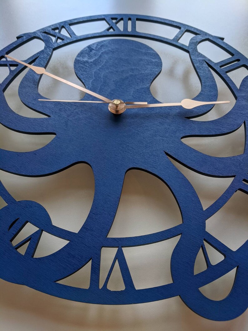 May include: A navy blue wooden wall clock with an octopus design. The clock has copper-coloured hands and Roman numeral hour markers. The octopus is the central design element, with its tentacles forming the clock's face.