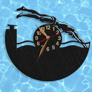 May include: A black and gold clock with a silhouette of a swimmer diving into a pool. The clock face has Roman numerals and a gold hand.