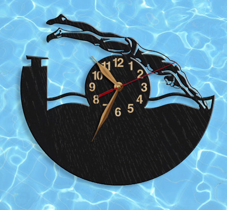 May include: A black and gold clock with a silhouette of a swimmer diving into a pool. The clock face has Roman numerals and a gold hand.