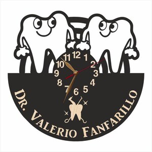 May include: Black and white clock with a dentist theme. The clock face features two cartoon teeth with smiling faces. The clock hands are red and gold. The clock is surrounded by a black circle with the text "Dr. Valerio Fanfarillo" in white.