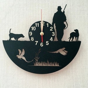 May include: Black and white silhouette wall clock featuring a hunter with a gun, two dogs, and two pheasants. The clock face has Roman numerals and a red second hand.