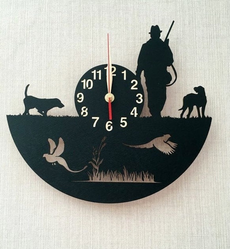 May include: Black and white silhouette wall clock featuring a hunter with a gun, two dogs, and two pheasants. The clock face has Roman numerals and a red second hand.