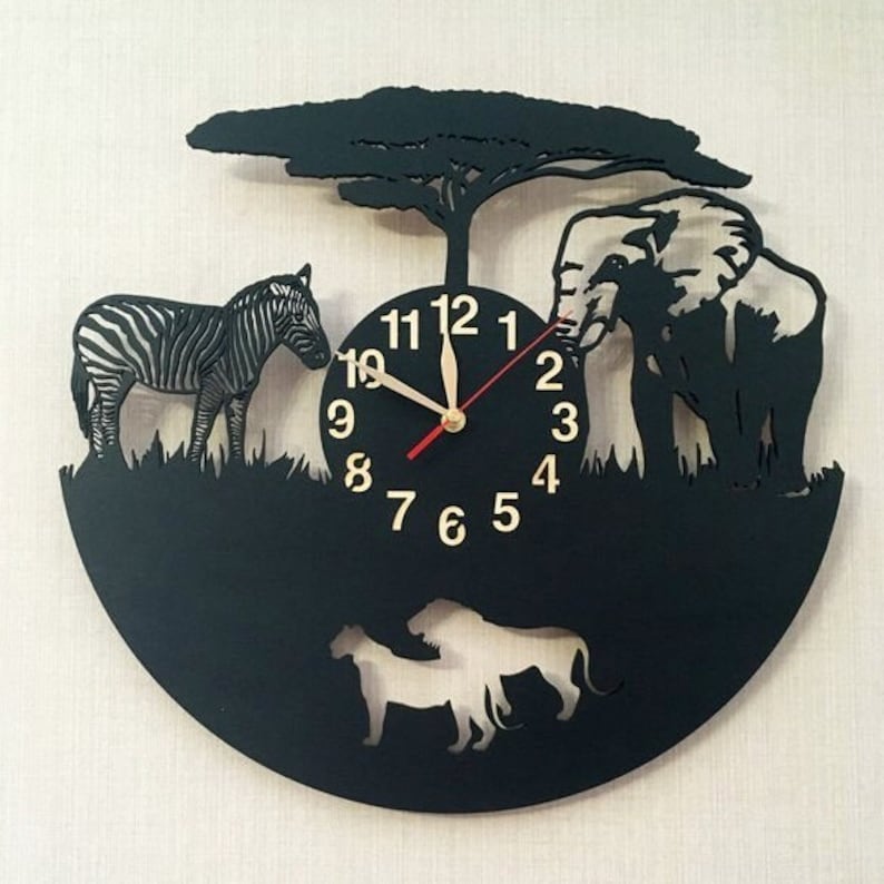 May include: Black vinyl record clock with a silhouette of a zebra, elephant, lion, and tree. The clock face has gold numbers 1-12 and black hands. The clock is on a beige background.