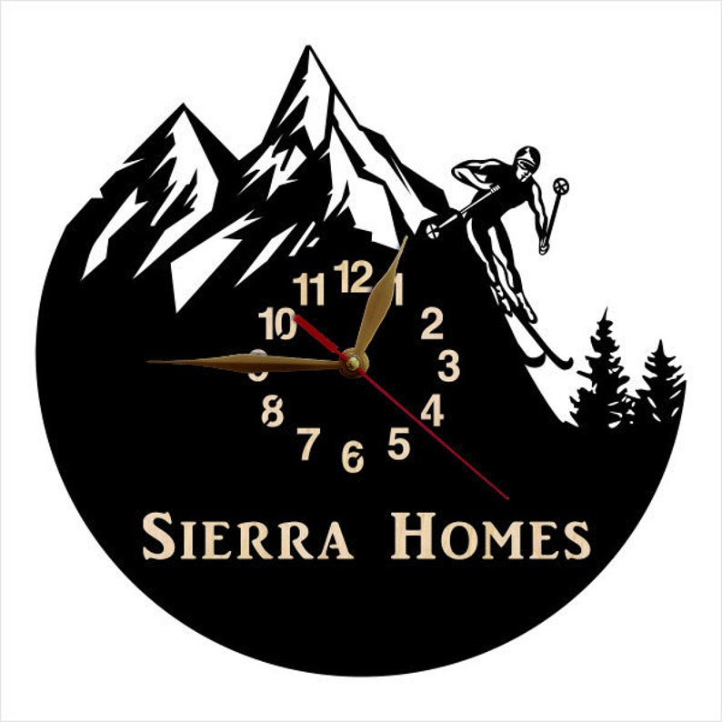 Puede incluir: Reloj en blanco y negro con una escena de monta&ntilde;a y un esquiador. La esfera del reloj tiene n&uacute;meros y manecillas dorados. El texto "SIERRA HOMES" est&aacute; en la parte inferior del reloj.