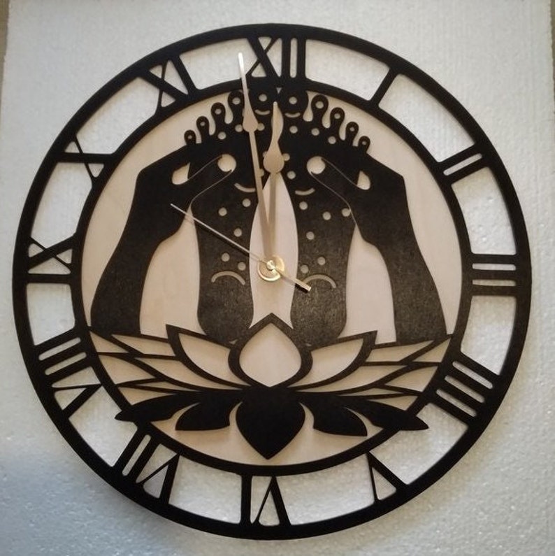 May include: Black and white wall clock with Roman numerals and a design of two feet with hands holding them, resting on a lotus flower.