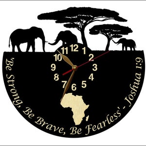 Puede incluir: Reloj negro con un contorno dorado y un mapa de &Aacute;frica dorado en el centro. La esfera del reloj tiene n&uacute;meros blancos y manecillas doradas. El reloj est&aacute; rodeado de un fondo negro con el texto "Be Strong, Be Brave, Be Fearless' - Joshua 1:9" en letras doradas.