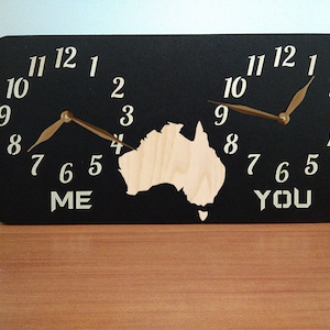 May include: A black wooden clock with two clock faces, one labelled "ME" and the other labelled "YOU". The clock faces are separated by a cutout of the continent of Australia. The clock hands are gold.