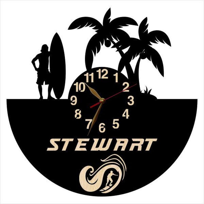 May include: A black wall clock featuring a silhouette of a person standing with a surfboard next to palm trees. The clock face has light-colored numbers, the name STEWART in capital letters, and a graphic of a person surfing inside a wave.